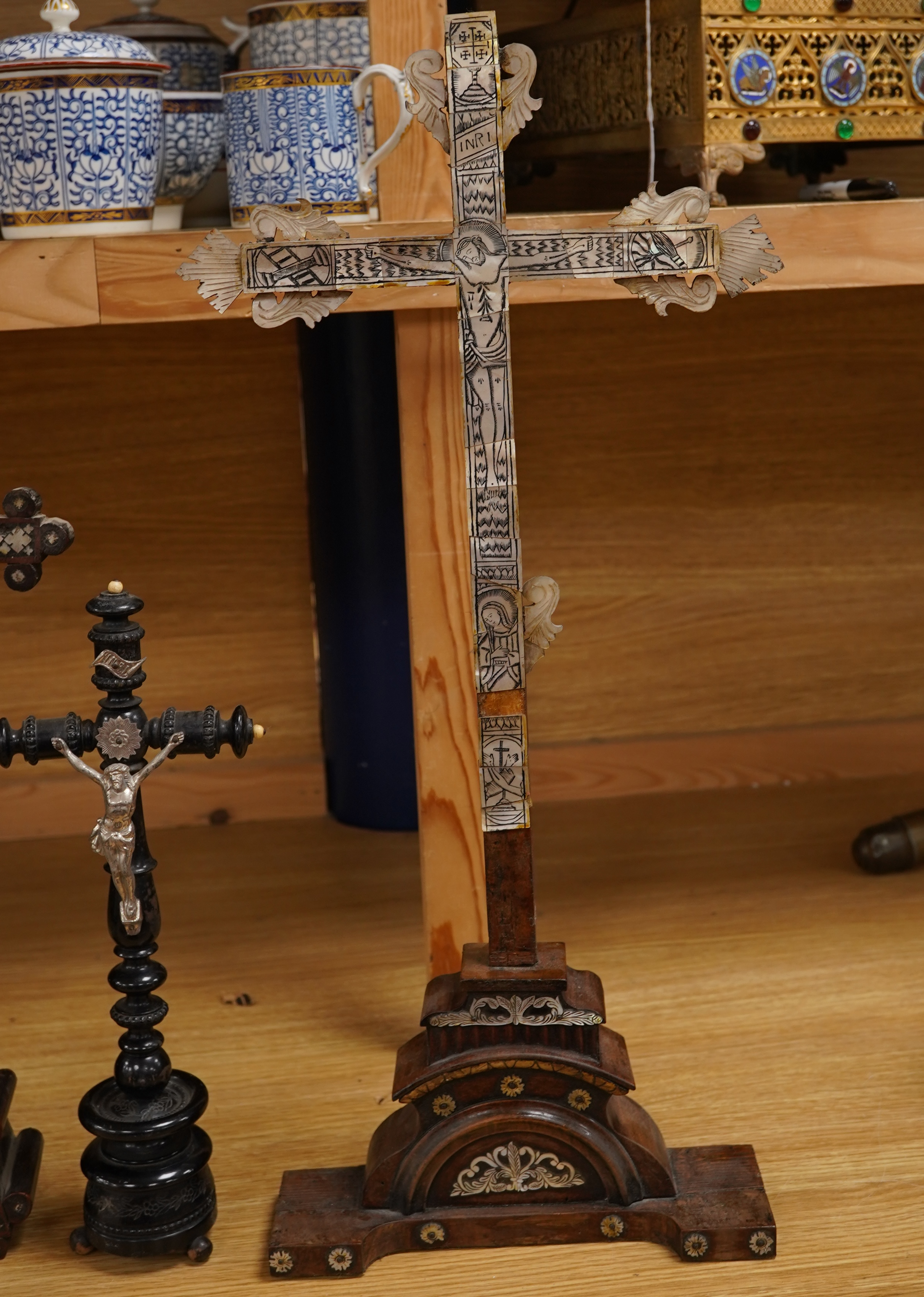 Two 19th century walnut and mother-of-pearl inlaid crucifixes and a German ebonised and white and metal mounted crucifix and a pair of Dutch or German brass tripod base cricket candlesticks, largest 56cm high (5)